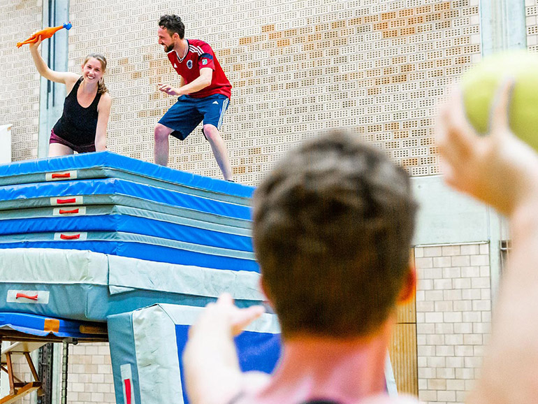 Drei Personen spielen ein Völk in einer Sporthalle